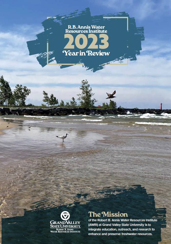 GVSU AWRI 2023 Year in Review magazine cover depicting a lakeshore scene with seagulls at a beach while trees sway from the wind. In the far distance, a red lighthouse is seen on a pier and white clouds streak across a blue sky.